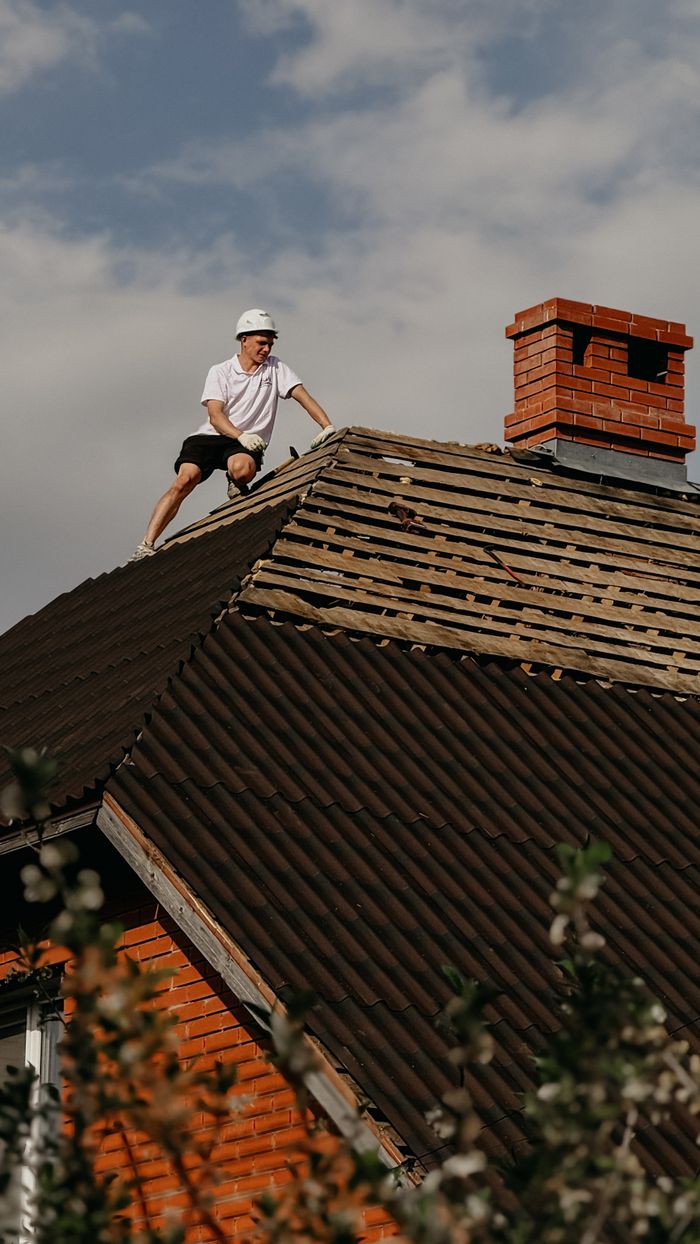about-01 Man in safety helmet repairing roof of red brick house under clear sky.
